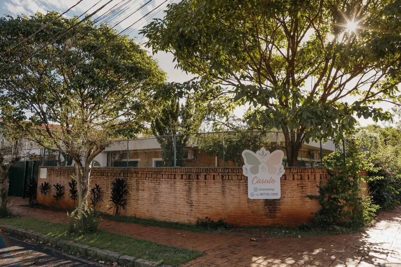 Fachada do Espaço Casulo vista da calçada, com muro de tijolos e jardim